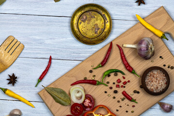 Fresh chopped vegetables, spices and seasonings kitchen utensils, cutting board on a white wooden background.