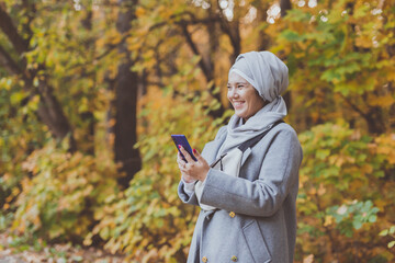 Pretty muslim woman using mobile phone outdoor. Arabic female wearing hijab using smartphone. Islamic girl texting a message phone in city park. Copy space