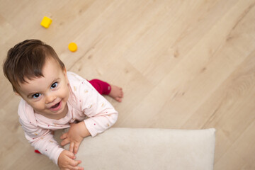 Happy toddler girl leaning on chair to stand up while is looking up and laughing. Positive concept. Copy space. 