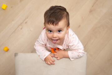 Top view of a baby girl leaning on a chair while looking at the camera and sticking out her tongue. 