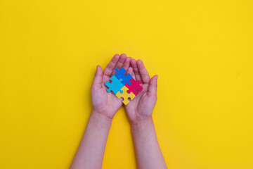 World autism awareness day. The hands of a small child holding colorful puzzles on yellow...