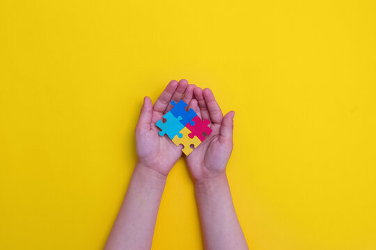 World autism awareness day. The hands of a small child holding colorful puzzles on yellow background. Copy space. Banner. Flat lay