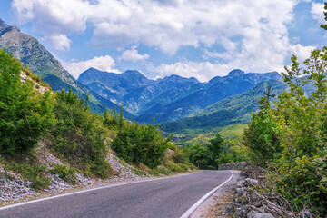 Fototapeta premium Summer landscape - valley and road in Albanian mountains, green trees and gray clouds on the sky
