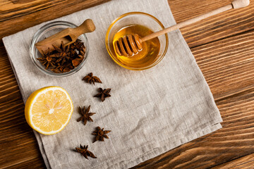 top view of honey and dipper near anise seeds and fresh lemon on linen napkin and wooden table