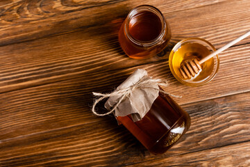 top view of honey jars and bowl with dipper on brown wooden surface