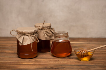 jars with fresh honey near bowl with dipper on wooden table and grey stone background