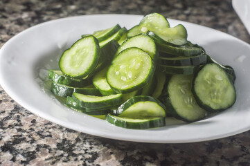 Cucumber pickles on a white plate with dark background and copy space.