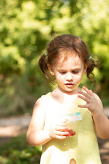 Little curly redhead girl holding a plastic glass with berries in her hands on a blurred rustic background with bokeh