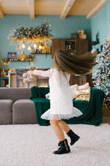 A cute girl holds a soft toy in her hands and dances with it, spinning in a room decorated for Christmas, against the background of a Christmas tree