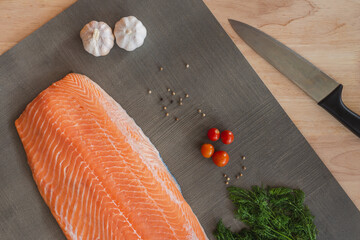 Fillet of salmon side with tomato, garlic, black pepper,dill and kitchen knife. Salmon is delicious and healthy fish. Salmon is famous in the world it can use in western food and eastern food.