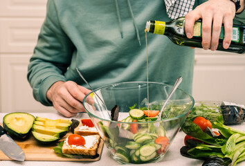 A man in the kitchen of the house cooks a healthy meal of vegetables with olive oil.