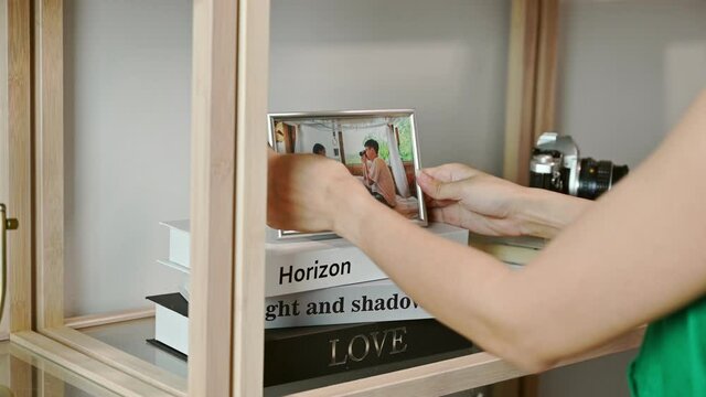 Female hand arranging and putting couple photo frame on book at wooden shelf