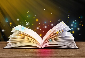 Magical image of open antique book on wooden table with glitter lights