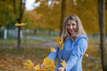 Fototapeta na wymiar Young beautiful blonde girl in an autumn park in the maple leaves. 