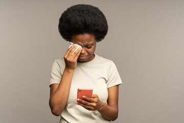 Young woman cry reading sms on smartphone. Unhappy black female getting bad news in mobile phone message notification sobbing and wiping tears with napkin. Life troubles, crisis and breakup concept