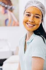 The process of applying a cosmetic mask on the face of a young girl who came to a beauty salon. Portrait of a happy satisfied customer