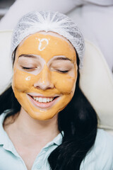 The process of applying a cosmetic mask on the face of a young girl who came to a beauty salon. Portrait of a happy satisfied customer