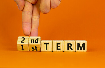 First or second term symbol. Businessman turns wooden cubes and changes words '1st term' to '2nd term'. Beautiful orange table orange background. Business and first or second term concept, copy space.