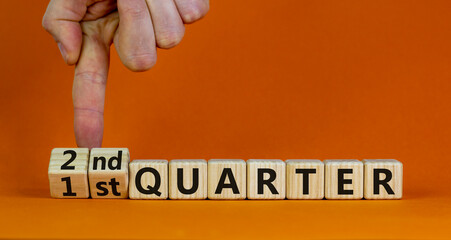 From 1st to 2nd quater symbol. Businessman turns cubes and changes words '1st quater' to '2nd quater'. Beautiful orange table, orange background. Business, happy 2nd quater concept, copy space.