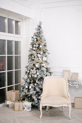 Classic white Christmas interior with decorated Christmas tree. Fireplace with beige armchair and gifts under the tree