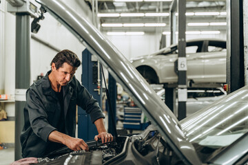 Process of repairing car after accident. Man working with engine near the car and examining it attentively. Stock photo
