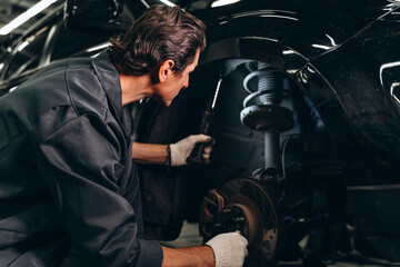 Obraz na płótnie Canvas Back view of car mechanic sitting near the broken car in auto repair service at the car service garage. Automobiles concept