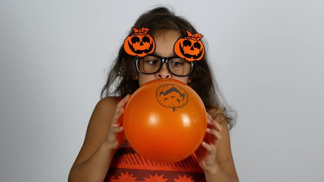 Happy Halloween. The girl inflates an orange balloon with a pumpkin pattern and enjoys the holiday.