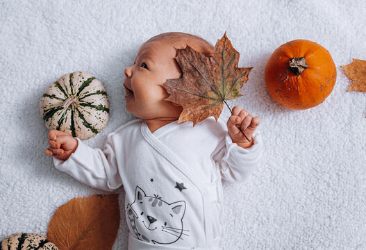 nursing baby infant in white clothes on a white background among pumpkins and autumn leaves