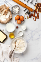 plate with wheat flour and ingredients for making dough for homemade cookies or gingerbread - eggs, milk, salt, sugar, butter, honey, spices (cinnamon, cardamom, anise) on a marble background