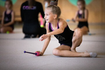 Girl gymnast doing exercise with clubs and smiling on training in gym