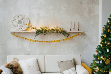 Christmas living room decor. Garland of dried oranges or lemons on the shelf above the sofa near the Christmas tree with lights.