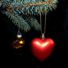 decorations for the Christmas tree. a Christmas toy in the form of a red heart and a gold one hang on a branch of a Christmas tree on a black background. side view