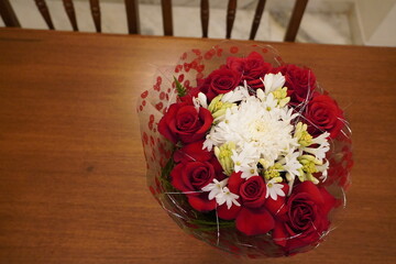 Bouquet of red roses and white flowers kept on a brown table. Beautiful bouquet of roses on table close-up. Table decor flowers in restaurant. Valentine's day background with red roses. Flat lay.