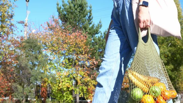 Woman walks with a braided string bag of fresh fruit. Life without plastic waste. Low-waste lifestyle. Sustainable ecological lifestyle