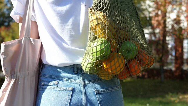 Woman walks with a braided string bag of fresh fruit. Life without plastic waste. Low-waste lifestyle. Sustainable ecological lifestyle