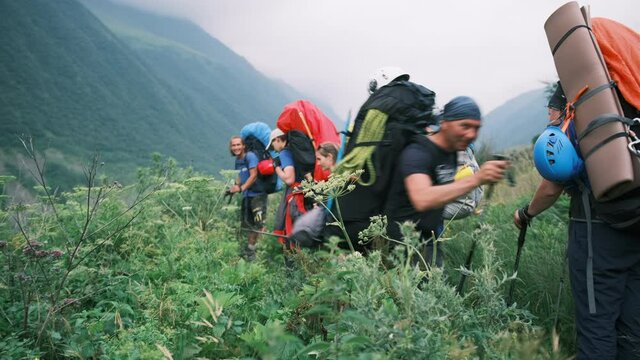 A group of hikers walks along the trail with huge backpacks with equipment in a mountain valley and gives way to a tourist going to a meeting. Tourists are walking along a trail in the mountains 