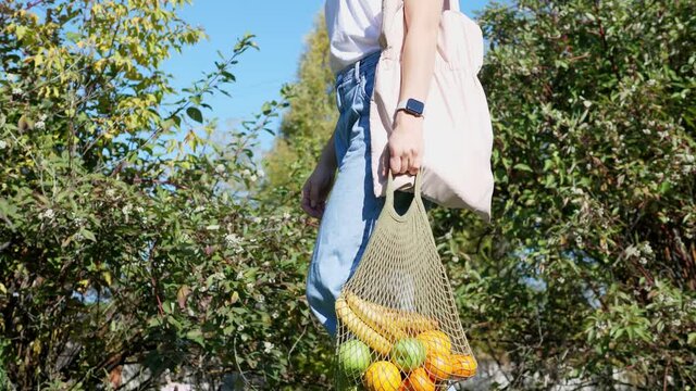 Woman walks with a braided string bag of fresh fruit. Life without plastic waste. Low-waste lifestyle. Sustainable ecological lifestyle