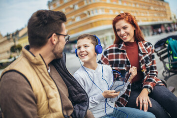 Fototapeta premium Family sitting on bench, relaxing using gadget, browsing internet.