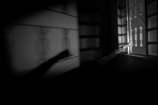Braços de uma pessoa segurando na janela. Imagem de mistério em preto e branco.