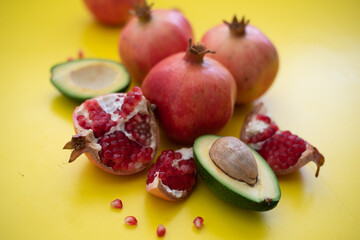 Three juicy and ripe pomegranates and avocado on yellow background. Fruits contain many vitamins. healthy fruits:  good for healthy lifestyle.  food for diet. jewish holiday. Close up.