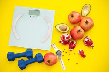Lot of pomegranates, cut avocado, weigher, dumbbells and sport watch on yellow background. Fruits contain many vitamins. healthy fruits:  good for body. food for diet. top view