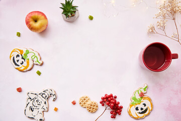 Halloween festive background: red cup, homemade cookies in shape of cute pumpkins and ghost. Atmospheric aesthetic autumn mood or trick or treat concept. Apples, dry flowers, candied fruit. Copy space