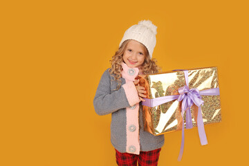 a little happy beautiful blonde girl in a white knitted hat and a knitted gray winter jacket holds a gift box in her hands