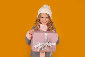 a little happy beautiful blonde girl in a white knitted hat and a knitted gray winter jacket holds a gift box in her hands
