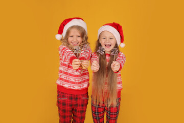 little beautiful happy blonde girls in a New Year's jumper in plaid trousers and Santa Claus hats are holding the numbers 2022 on a yellow background