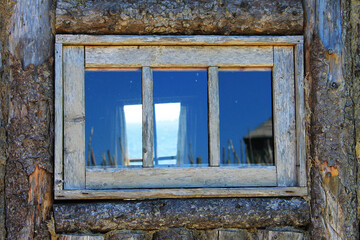 Looking in through an old, wood framed window in the wall of a log cabin, and out through the window on the opposite wall, at the Atlantic Ocean.