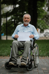 Adult disabled man in wheelchair holds paper sheet