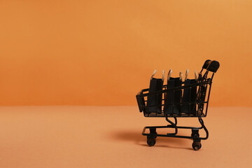 black paper bags in shopping cart on orange background, copy space. black friday concept