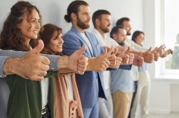 Group of successful business people doing like gesture all together. Team of ambitious confident young, mature and senior businesspeople standing in modern office, giving thumbs up and smiling