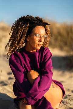 Chica con sudadera y pelo rizado en la playa al atardecer